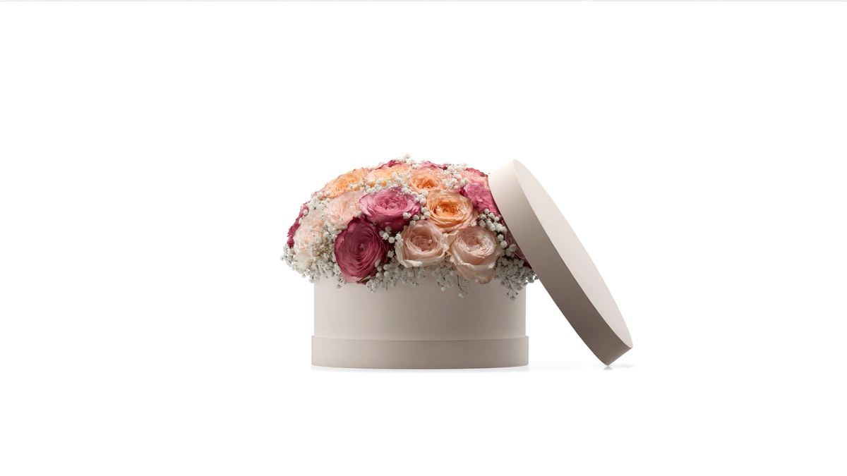 A round cream hat box filled with blush and peach roses on a white background