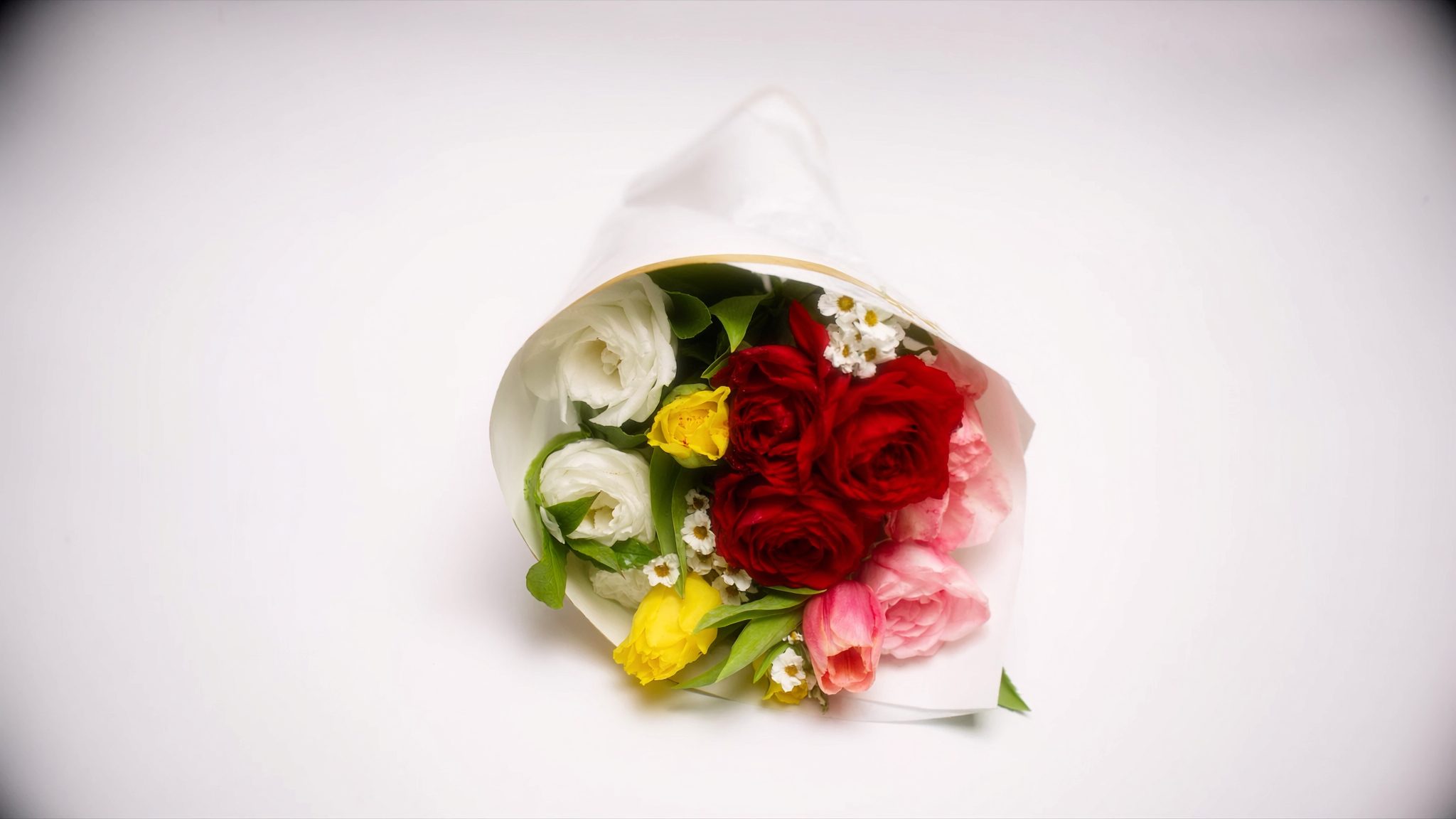 A colourful mixed bouquet of roses, tulips and gerberas on a white background