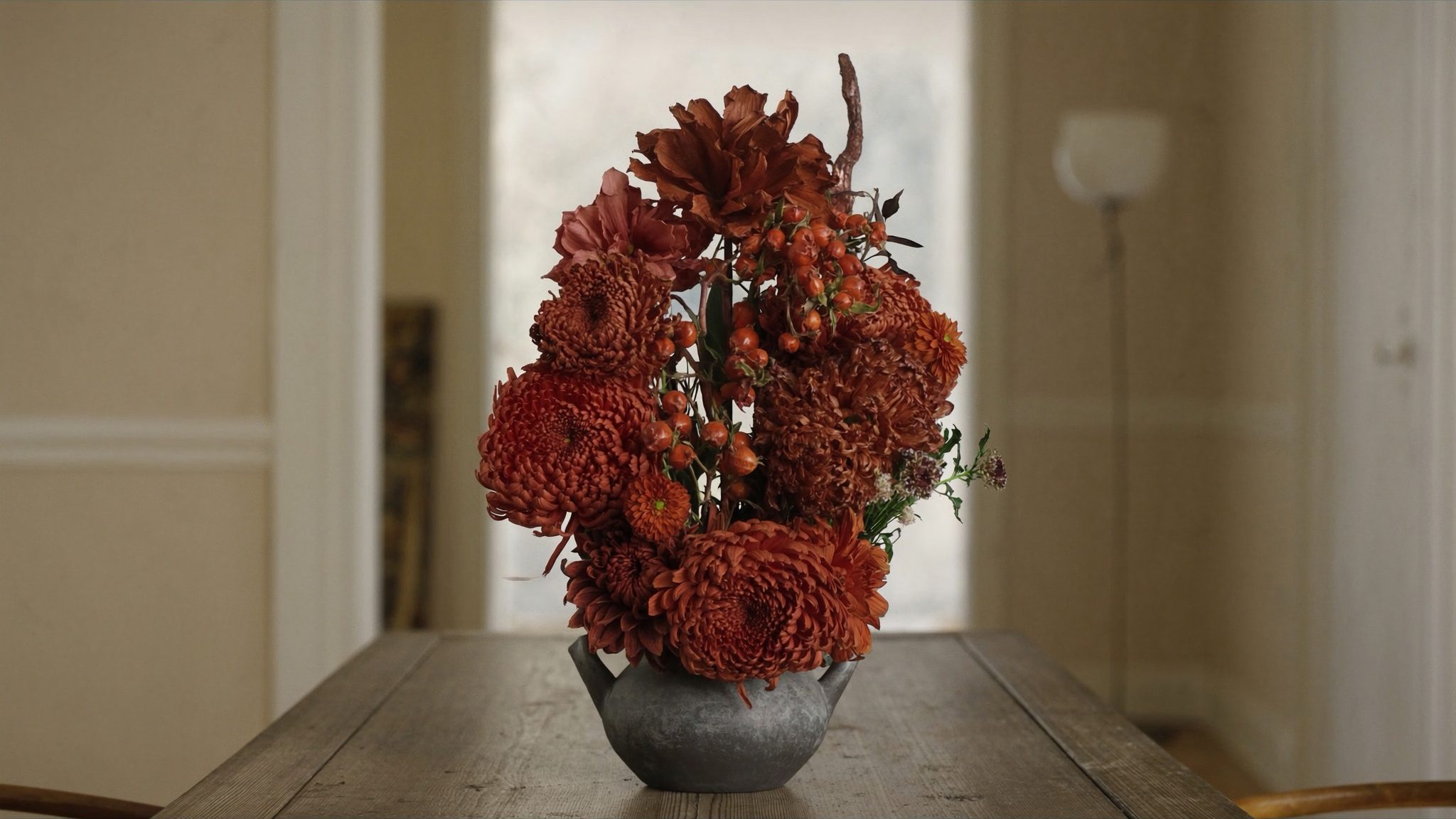 A rustic autumn arrangement of rust chrysanthemums and rose hip branches in a stoneware jug